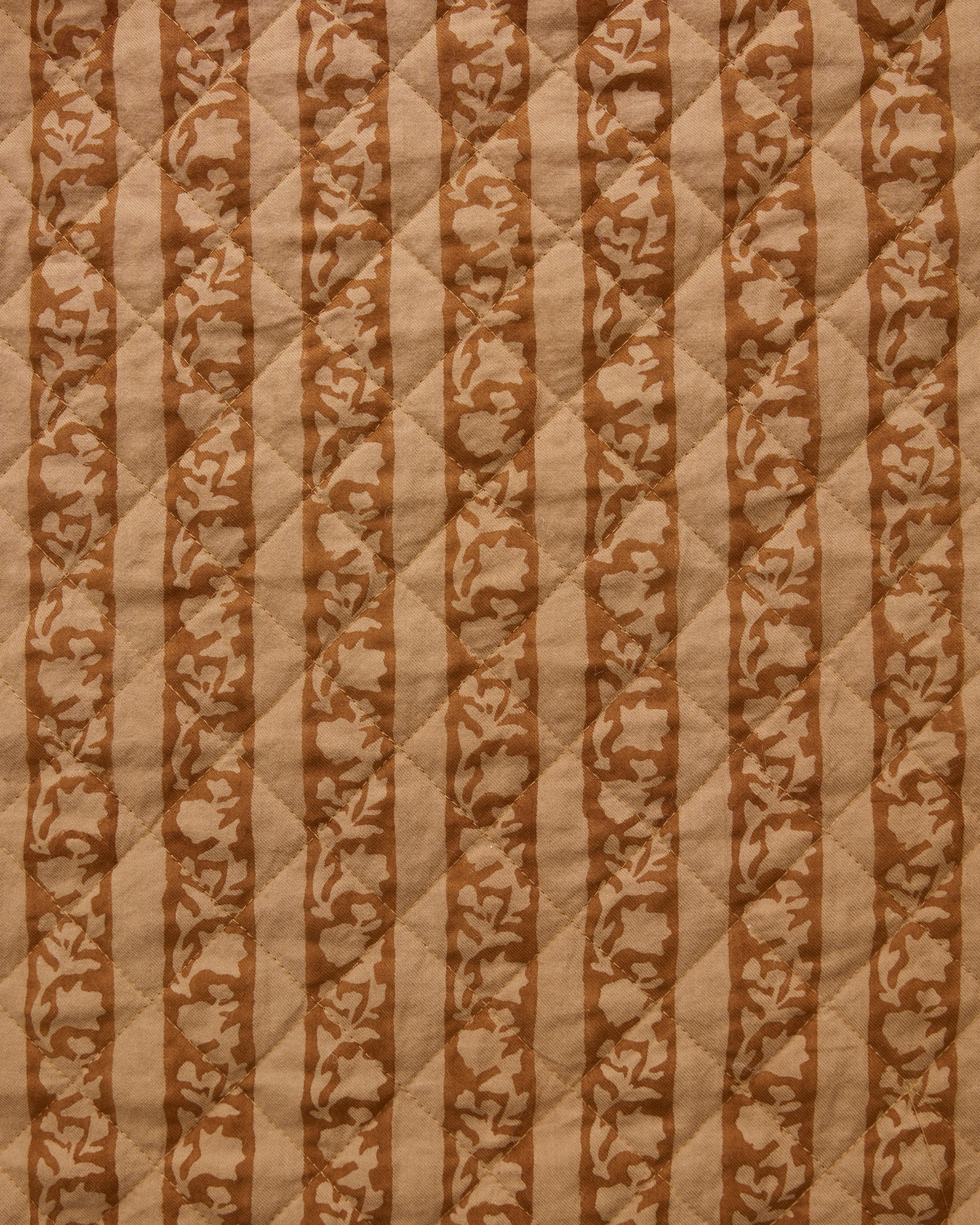 Close-up of quilted tan fabric with alternating vertical stripes and floral motifs.