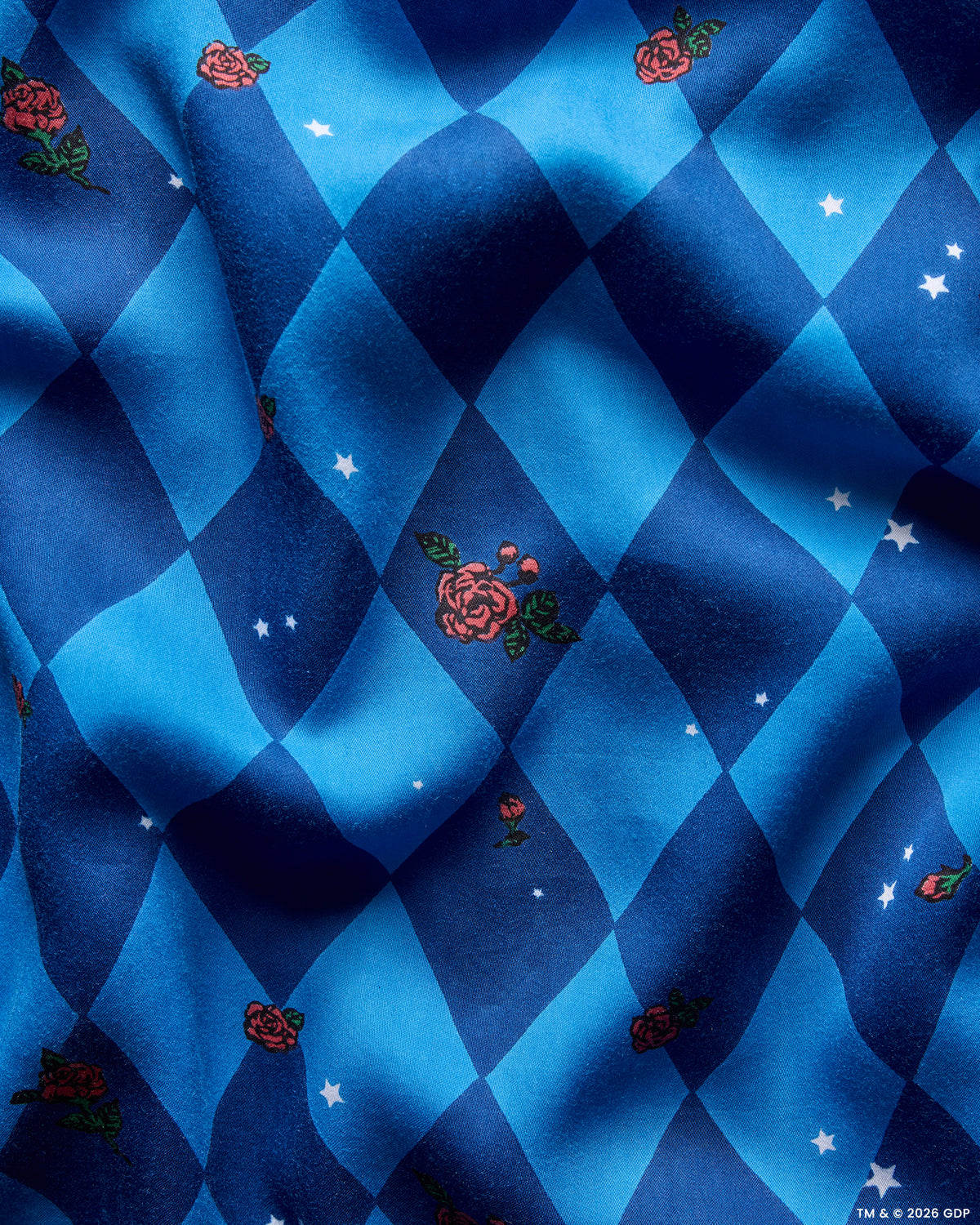 Close-up of the blue argyle print with scattered red roses, green leaves, and white stars.