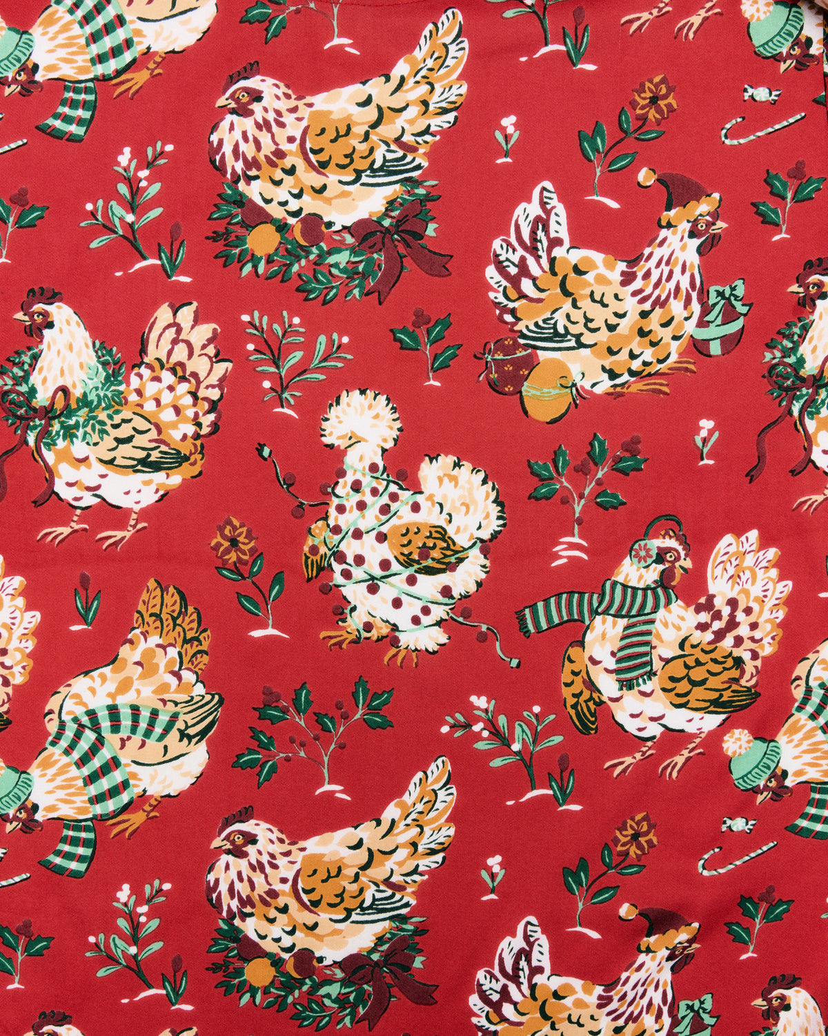 Close-up of red fabric with illustrated chickens in holiday clothing and greenery