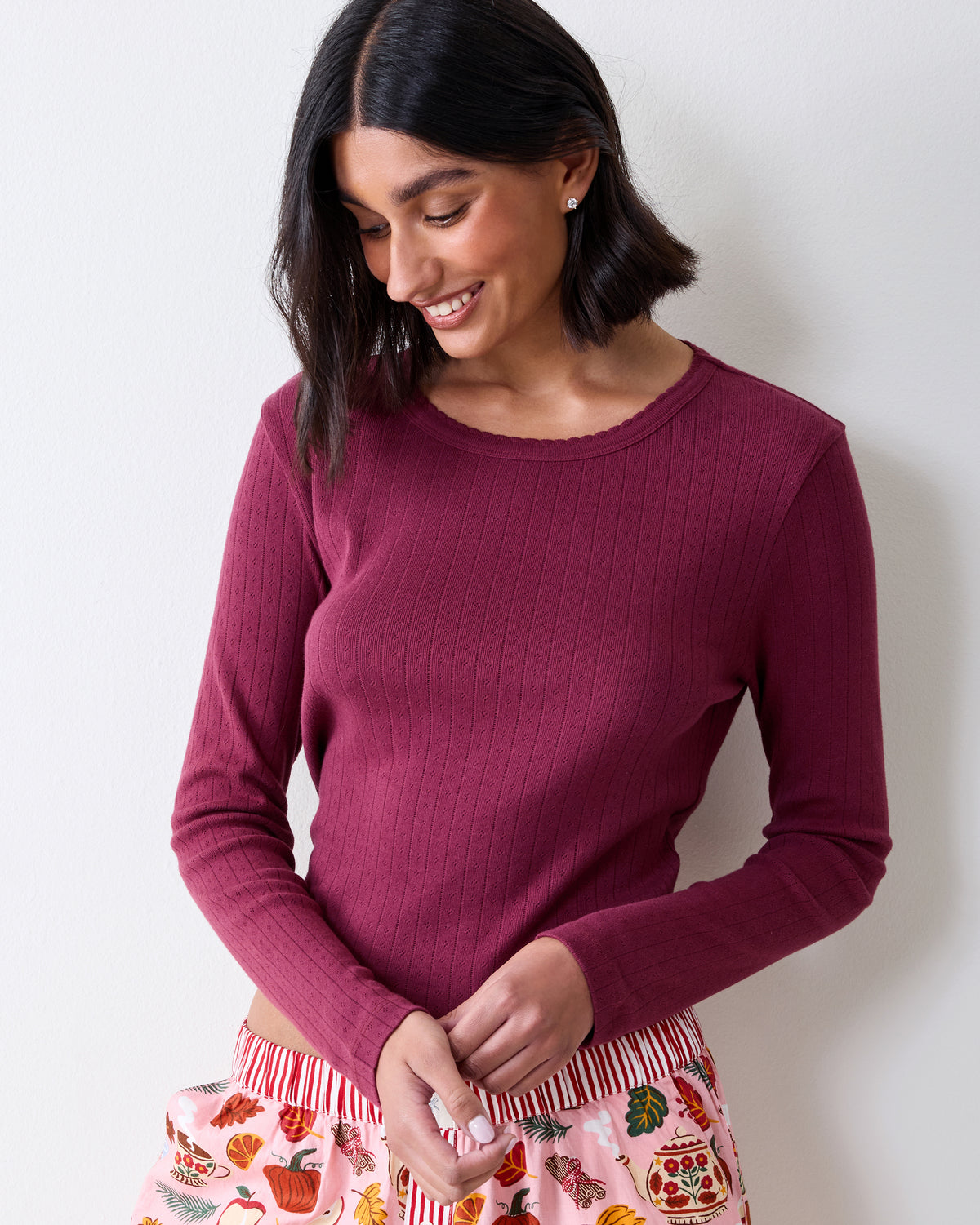 Three-quarter front view of a wine-colored long-sleeve pointelle top with a scalloped neckline and vertical eyelet pattern.