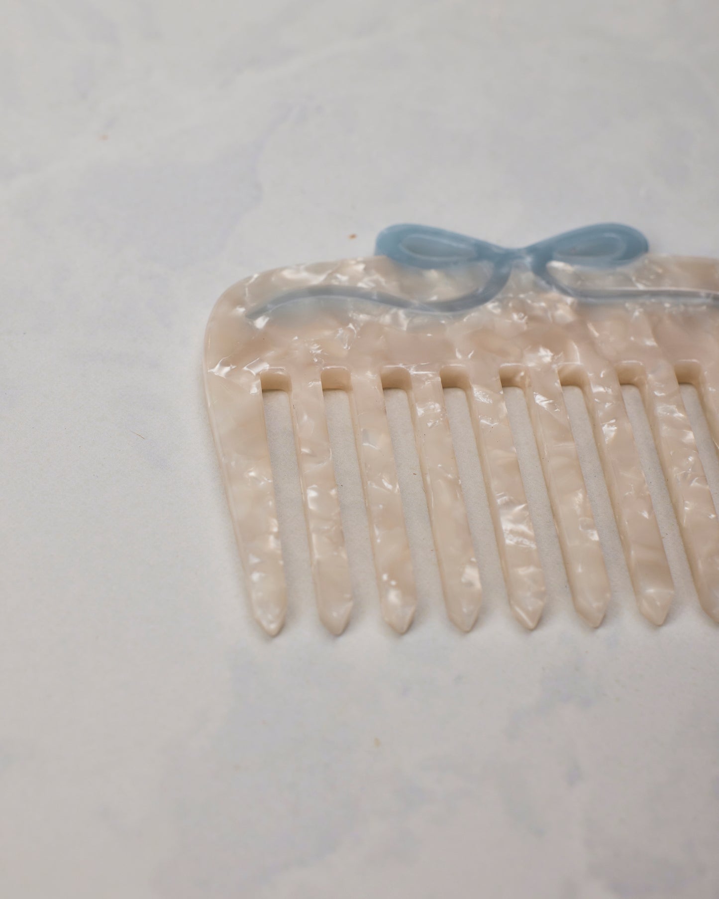 Close-up of the white wide-tooth pocket comb showing its pale blue bow detail and textured surface.