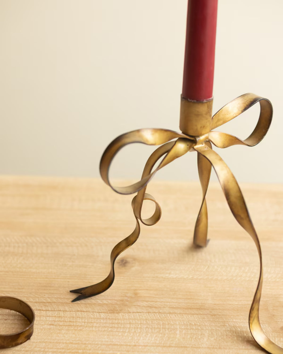Close-up of an antique brass bow taper candle holder with a red taper candle on a wooden table
