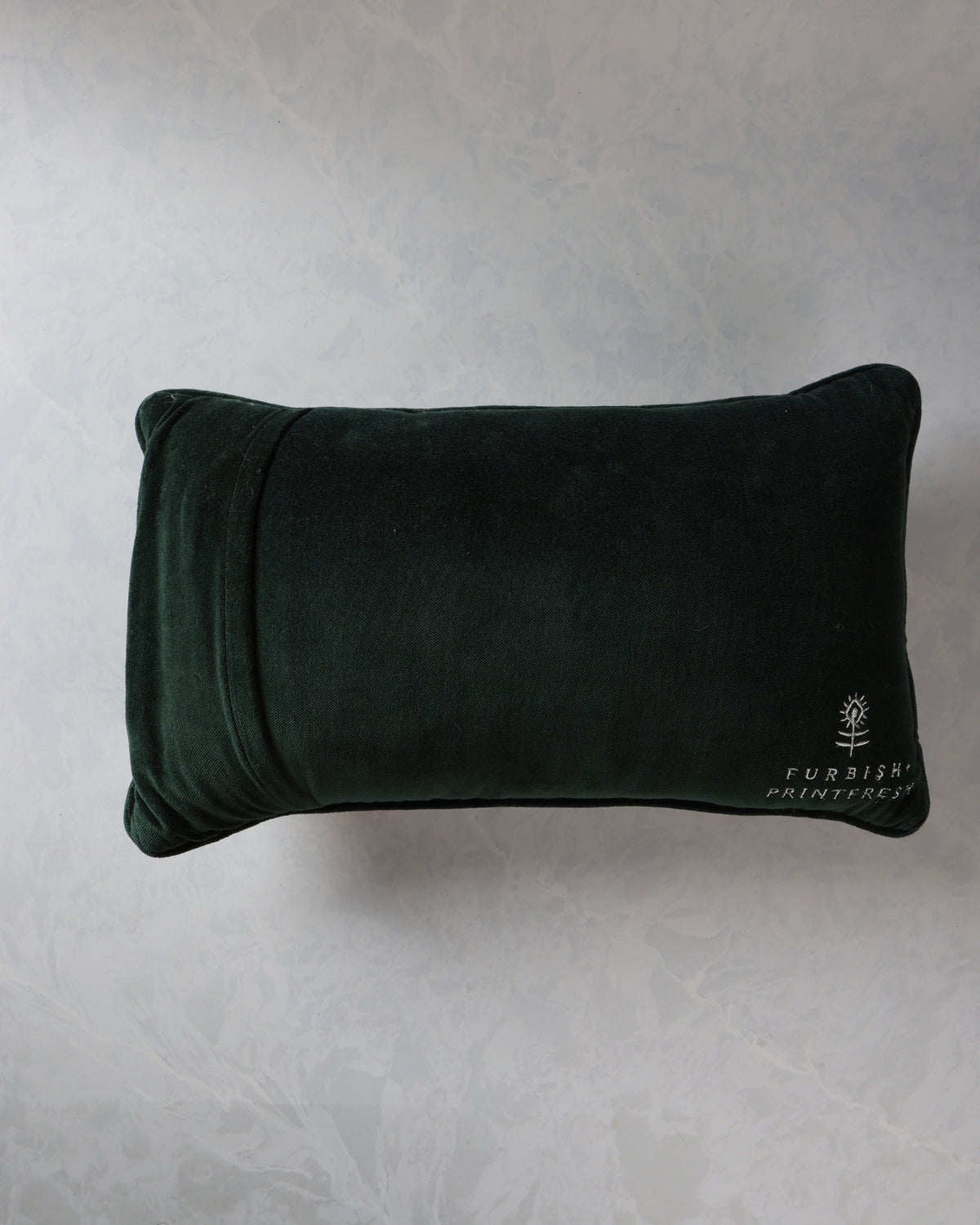 Reverse view of a dark green rectangular throw pillow with the Furbish Printfresh logo embroidered near the lower right corner.