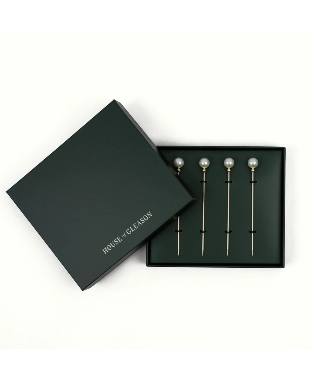 Four pearl cocktail picks displayed in a black presentation box beside its lid.
