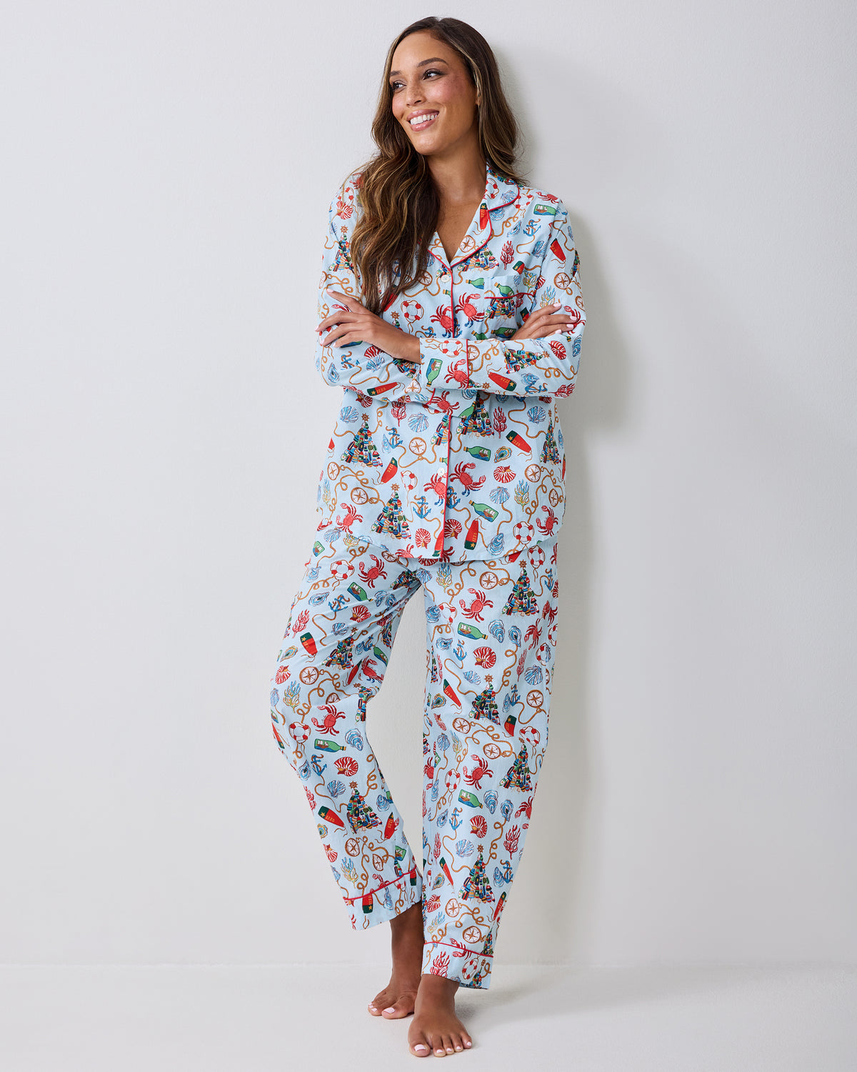 Adult wearing a light blue long-sleeve pajama set with a nautical Christmas print, standing barefoot against a light wall.