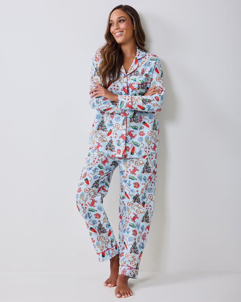 Adult wearing a light blue long-sleeve pajama set with a nautical Christmas print, standing barefoot against a light wall.