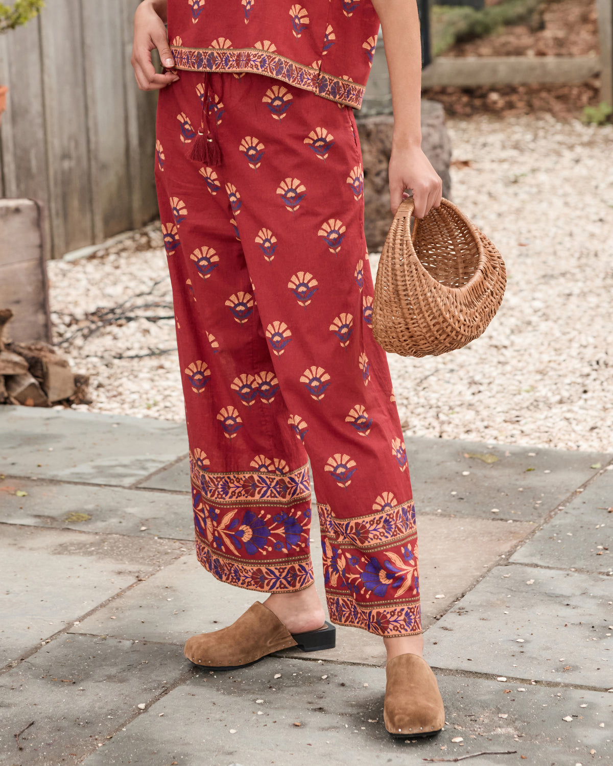 Close view of red rock Delia pants with wide legs, tassel-tie waist, pockets, and repeated floral fan print.