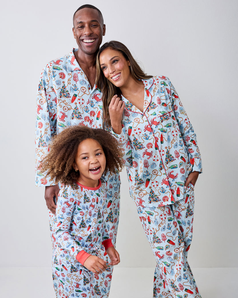 Adults and a child wearing matching Holidays Ahoy pajamas with a light blue nautical holiday print.