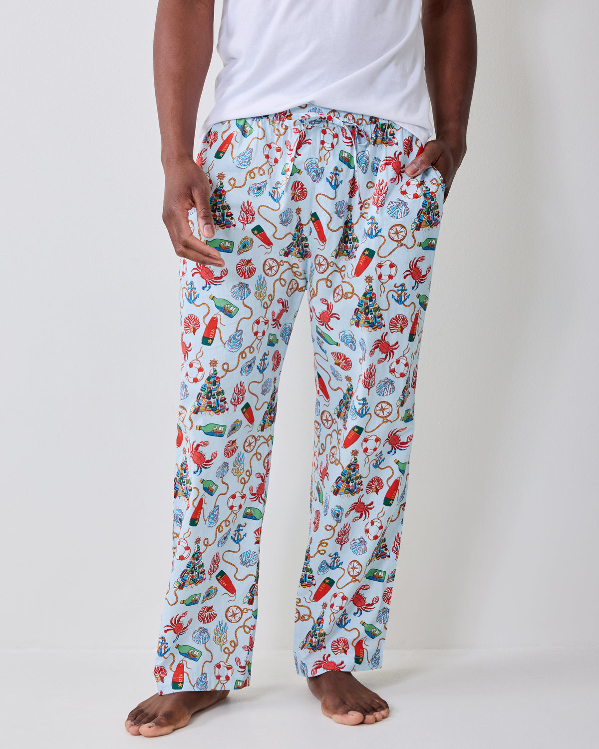 Front view of the men's long pajama pants with a light blue nautical holiday print and side pockets.