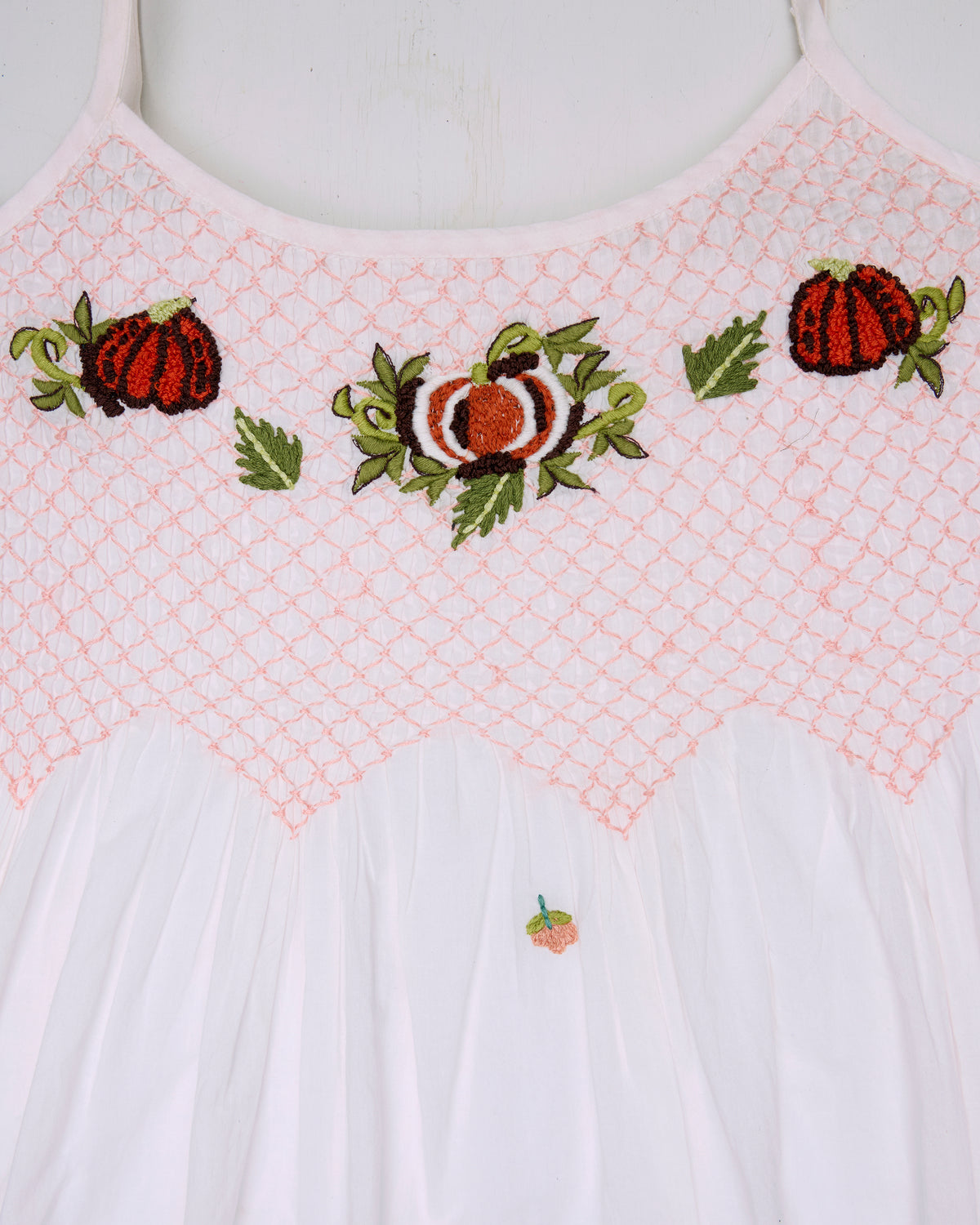 Close-up of a white nightie with a pink smocked yoke and embroidered pumpkin motifs.