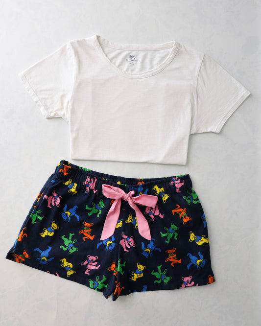 Flat lay of a white short-sleeve tee and navy pajama shorts with colorful dancing bear figures and a pink waist tie.