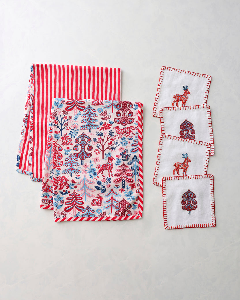 Tea towels and cocktail napkins arranged together, with red-and-white stripes, a forest print, and embroidered motifs.