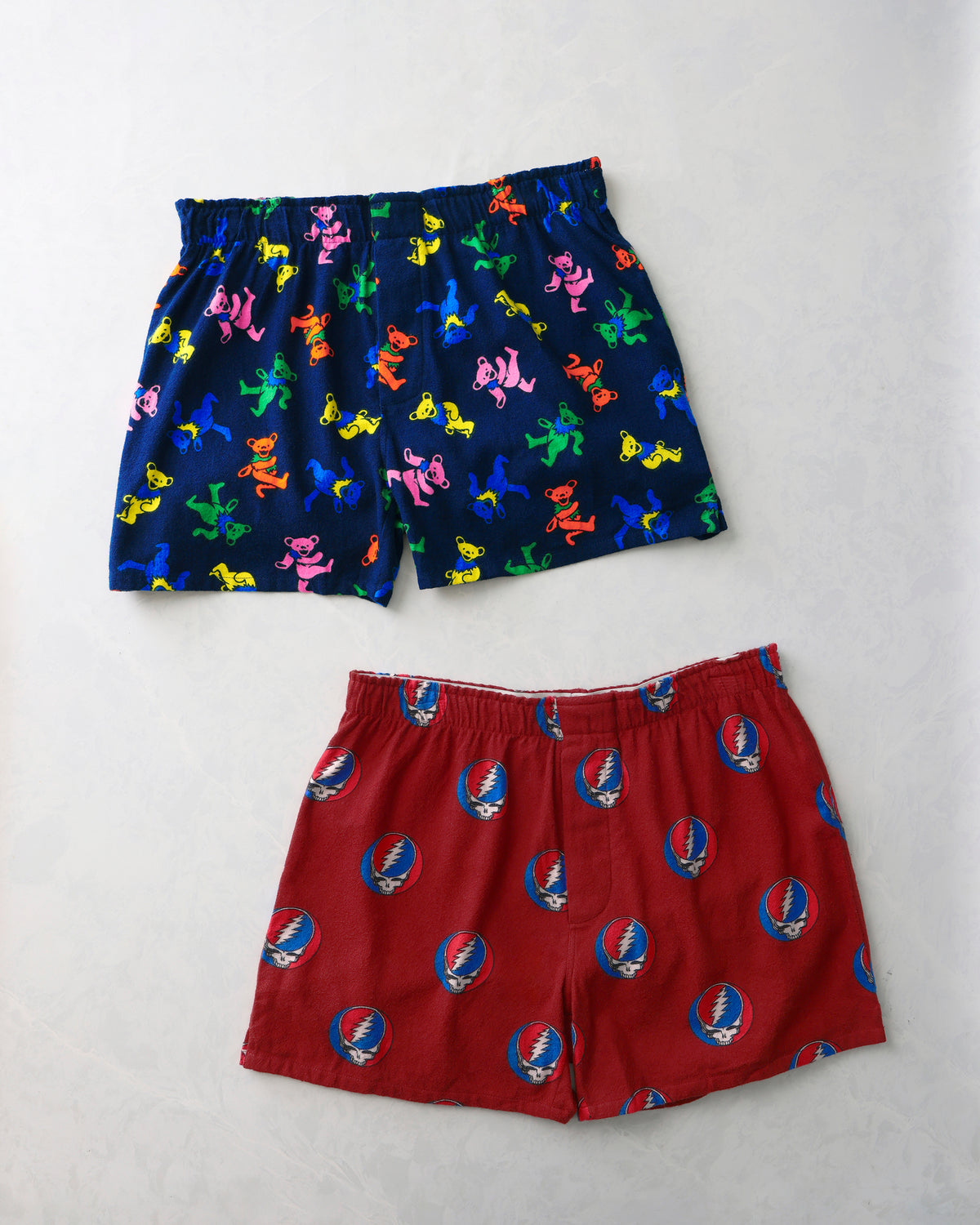 Two pairs of boxers laid flat: one navy pair with multicolored dancing bears and one red pair with circular skull-and-lightning-bolt emblems.