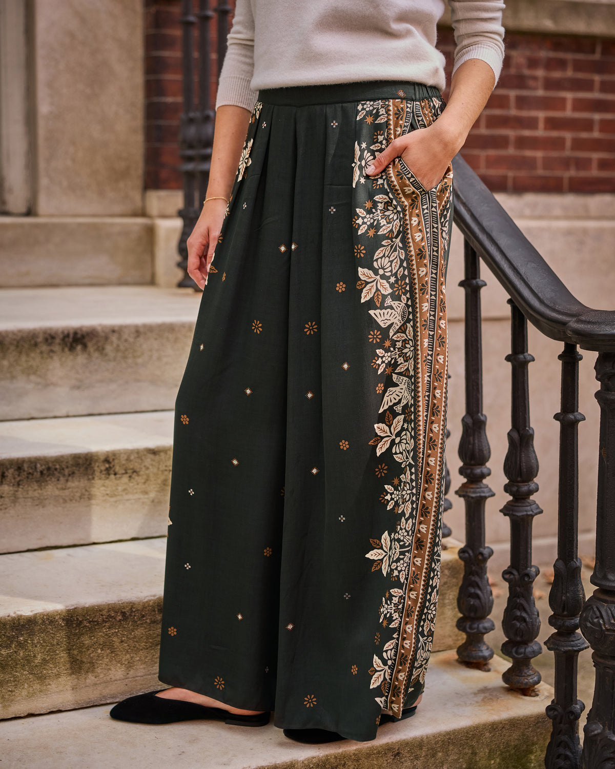 Spruce Sasha wide-leg pants with a floral tapestry print and contrasting patterned side border, shown on a model standing on steps.