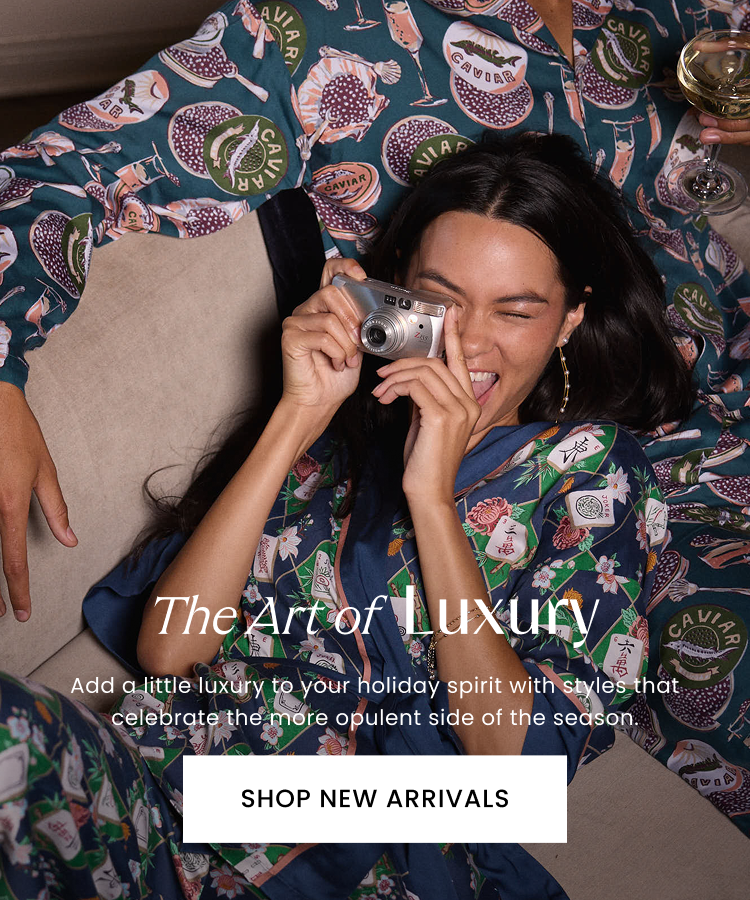 Person holding a compact camera while reclining in patterned clothing, with text reading “The Art of Luxury,” “Add a little luxury to your holiday spirit with styles that celebrate the more opulent side of the season,” and “SHOP NEW ARRIVALS.”