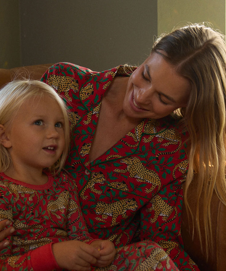 Two people seated together indoors, wearing matching red pajamas with repeating animal and leafy prints.