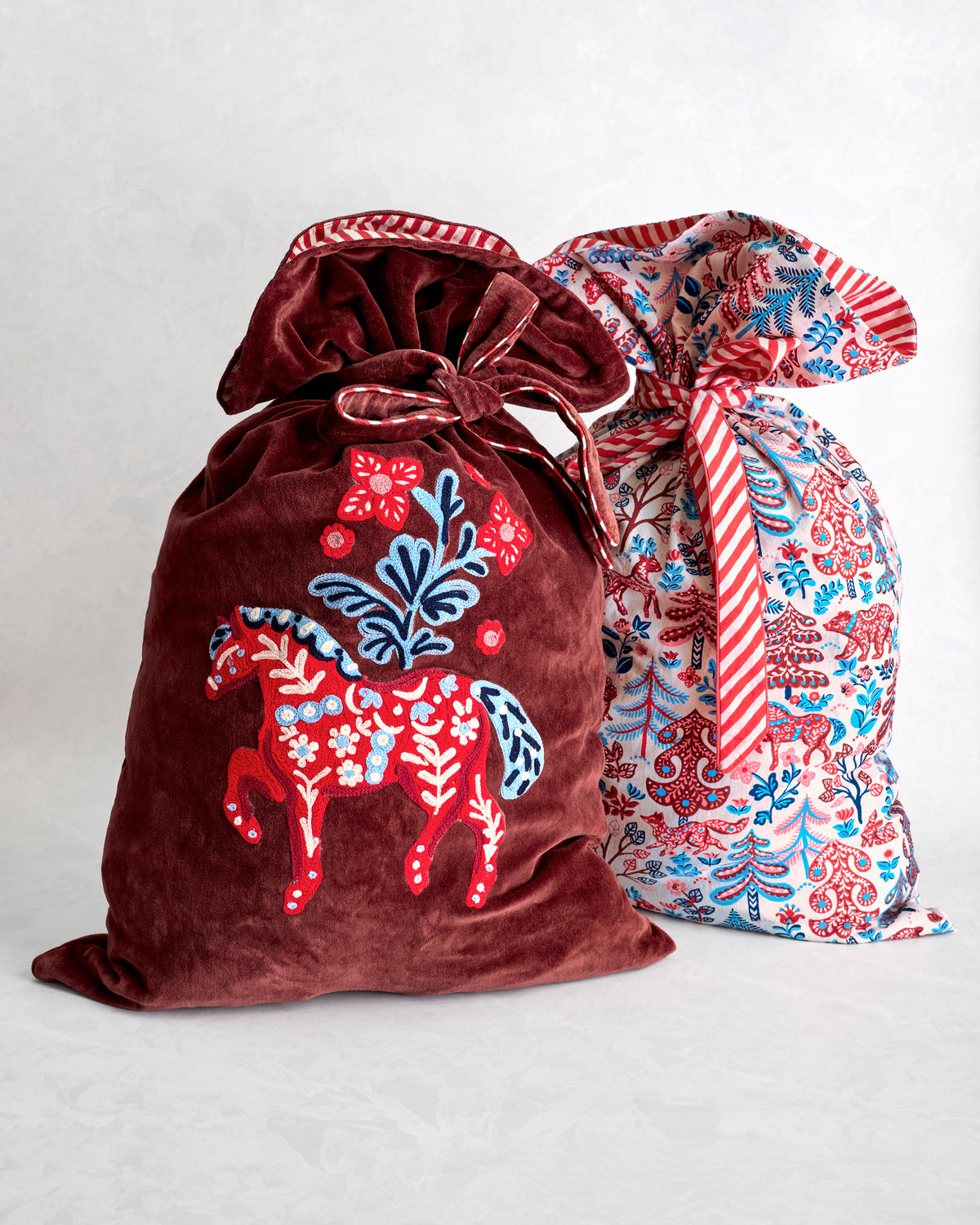 Two tied gift sacks, including a burgundy sack with an embroidered horse and a light patterned sack with red and blue motifs.