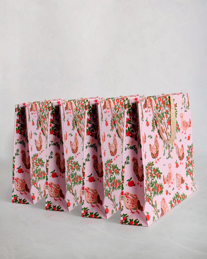 Set of four pink paper gift bags with chicken illustrations, foliage, and matching handles.