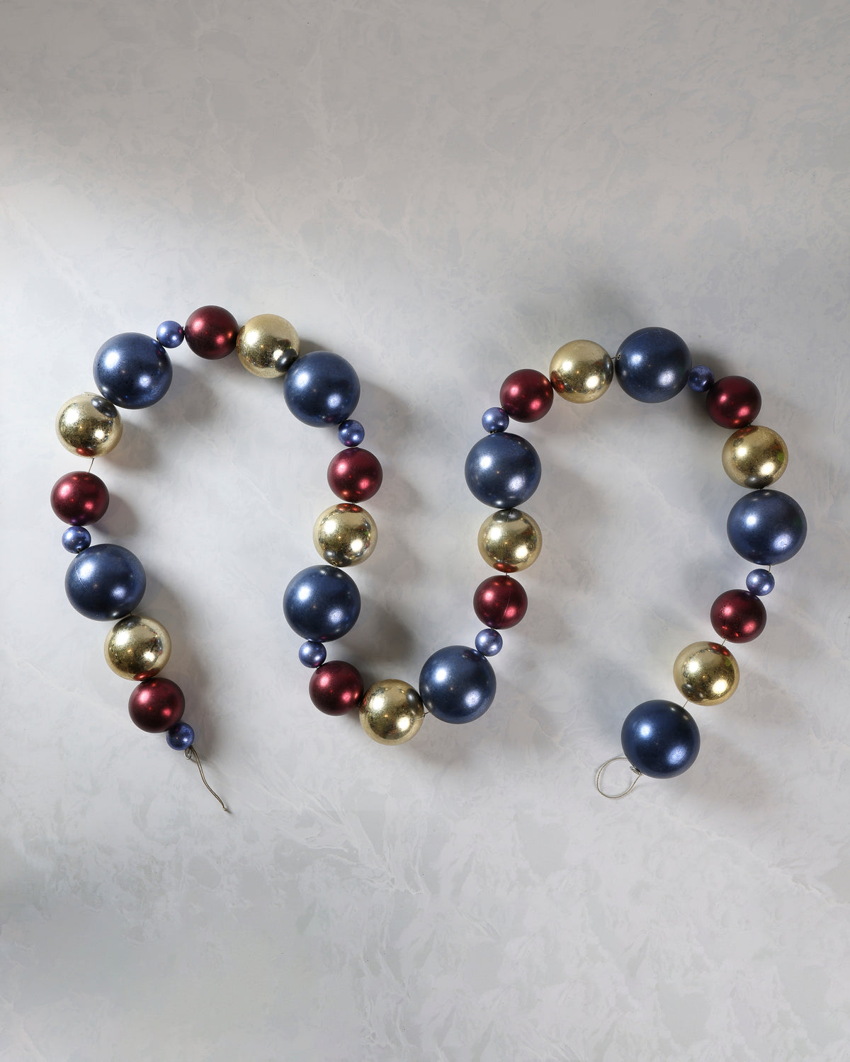 Burgundy, navy, and gold Christmas ball garland arranged in loops on a light background.
