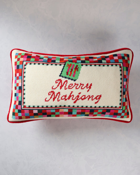 Rectangular needlepoint pillow with a multicolor border, green ornament motif, and red script reading “Merry Mahjong.”
