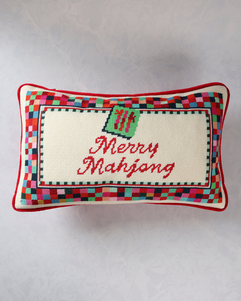 Rectangular needlepoint pillow with a multicolor border, green ornament motif, and red script reading “Merry Mahjong.”