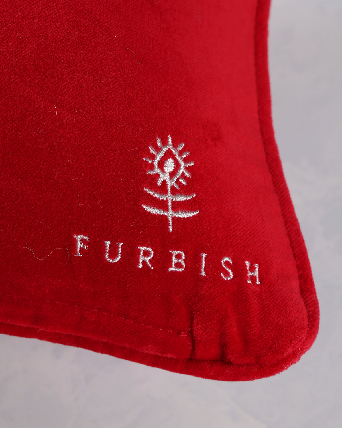 Close-up of the red pillow's lower-right corner showing the white Furbish logo and stitched edge.