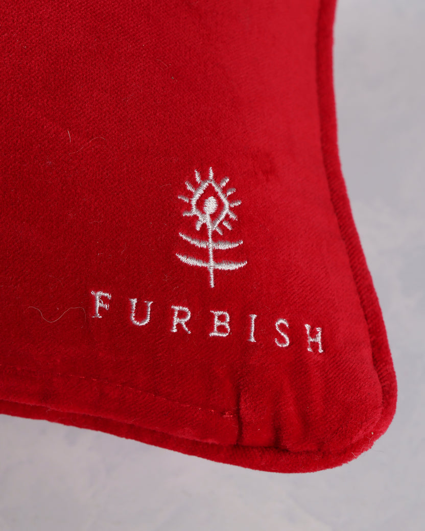 Close-up of the red pillow's lower-right corner showing the white Furbish logo and stitched edge.