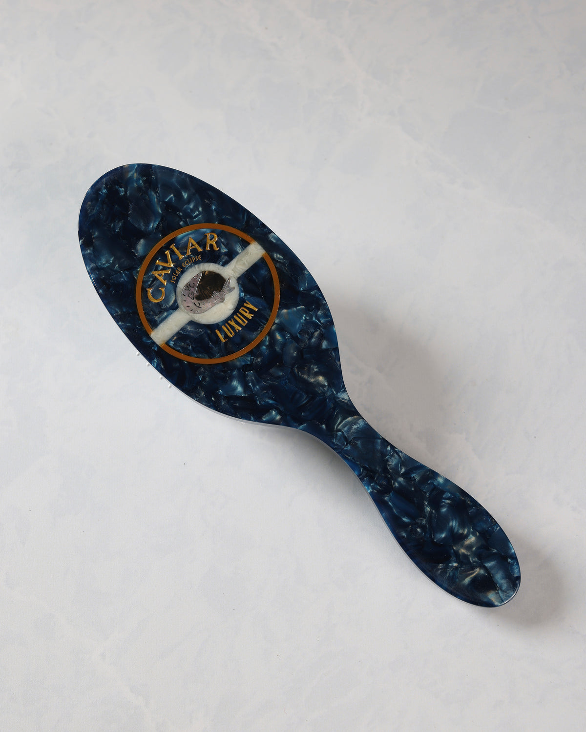 Full view of a dark blue patterned hair brush with a decorative circular emblem on the back.