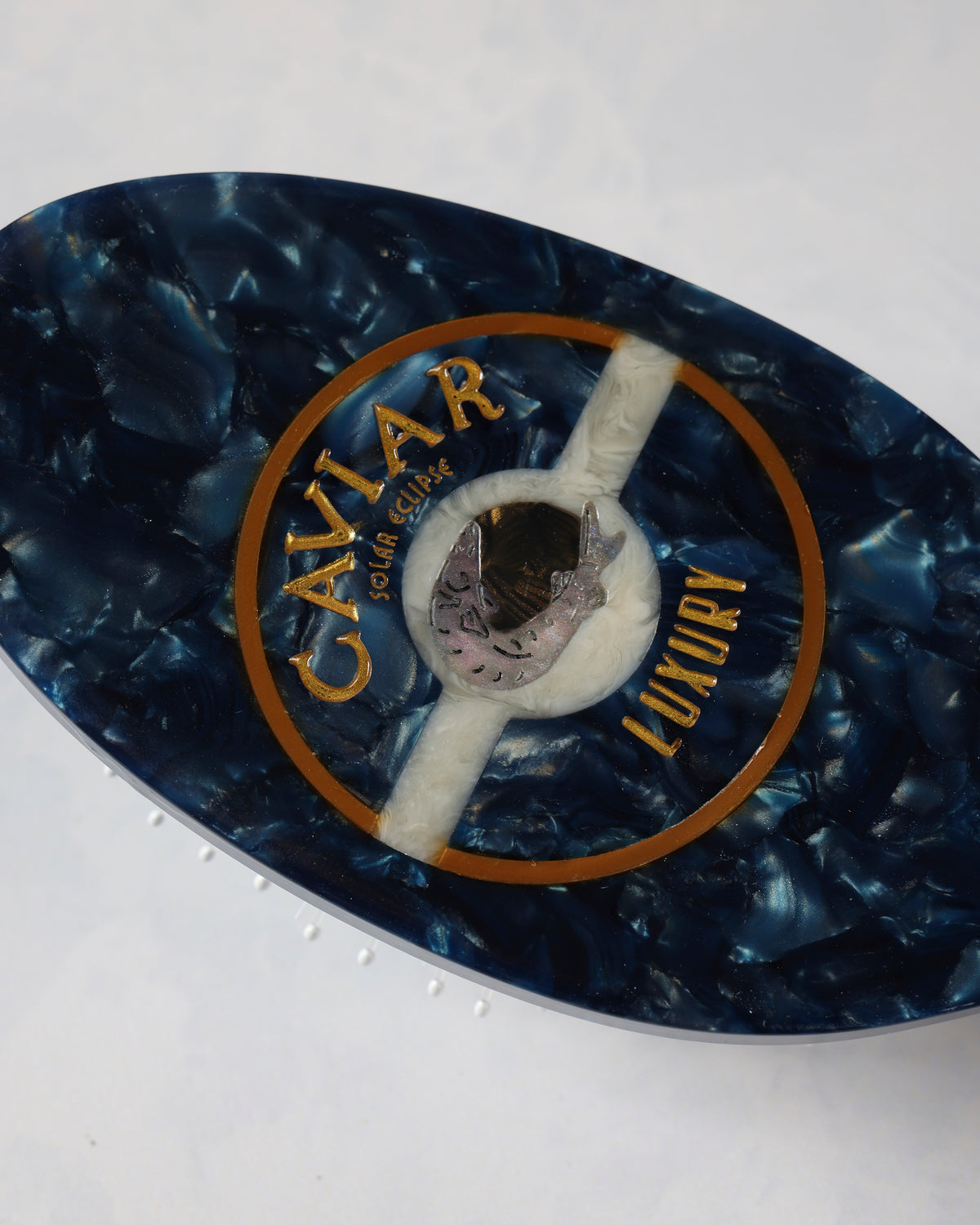 Close-up of the dark blue hair brush back showing its circular CAVIAR emblem.