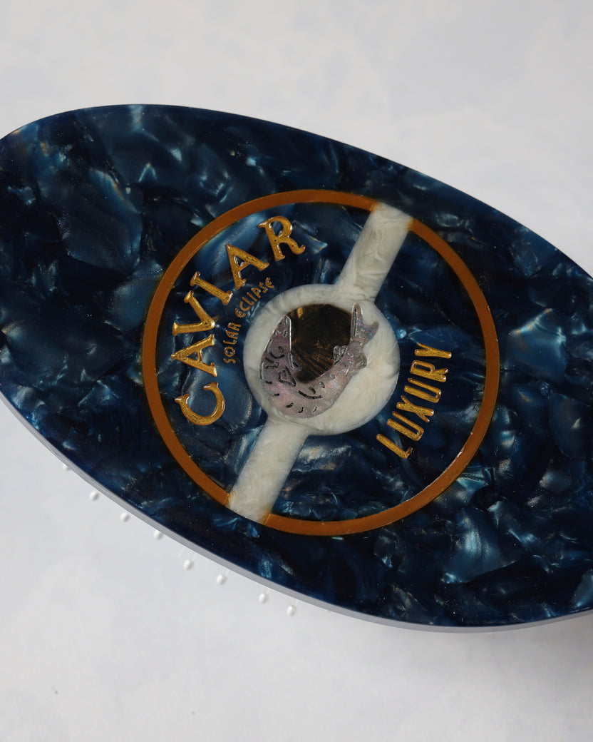 Close-up of the dark blue hair brush back showing its circular CAVIAR emblem.