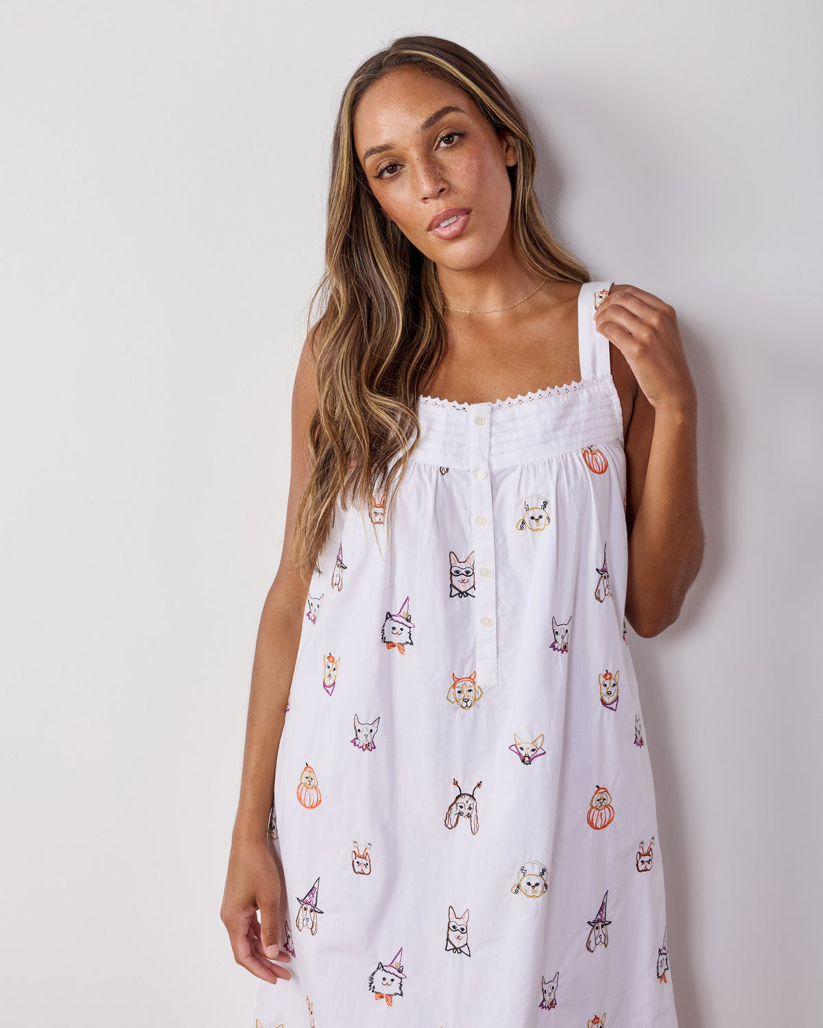 Front view of a white midi nightgown with shoulder straps, button front, and embroidered dogs in Halloween costumes with pumpkin motifs.