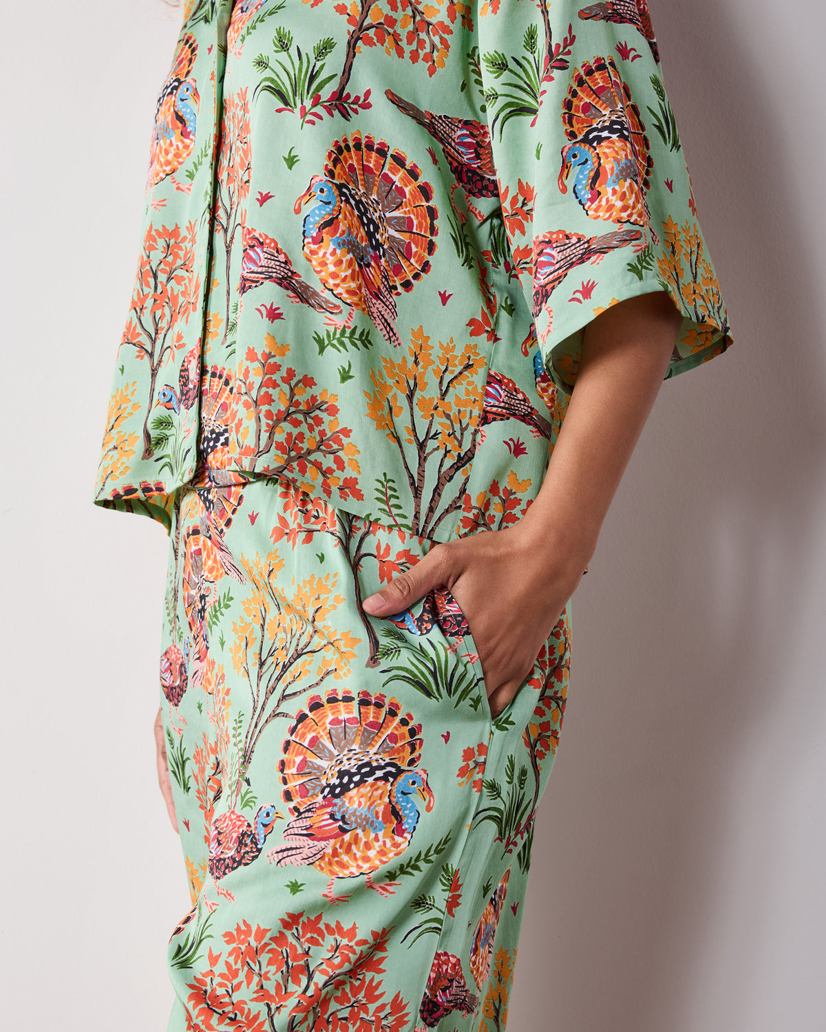 Side detail of the Soft Sage Turkey Trot Wildest Dreams pajama set, showing a hand in the pants pocket and the matching turkey-and-foliage print.