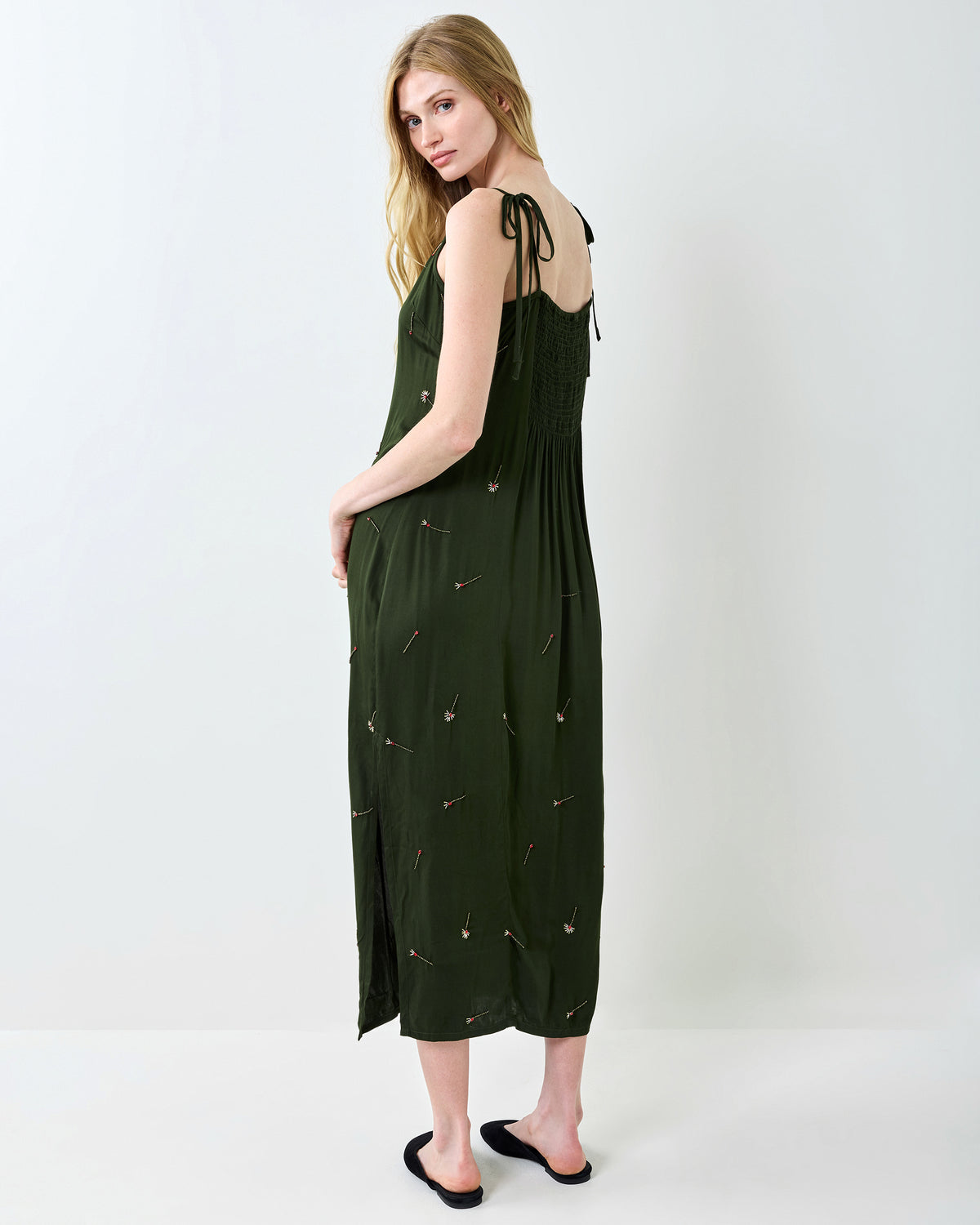 Back view of the olive Matchmaker Melody slip dress showing the smocked back, tie straps, and scattered decorative motifs.