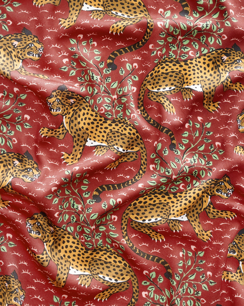 Close-up of the scarlet Bagheera robe fabric showing repeated leopard figures, leafy branches, and small white motifs.