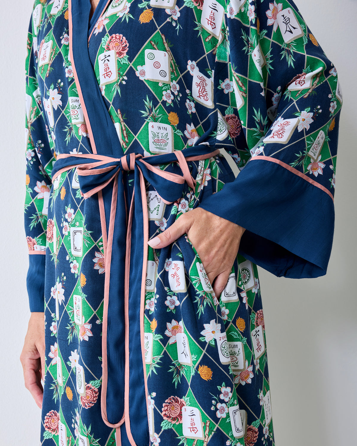 Close view of the wintergreen Mahj Garden robe showing the pink-trimmed waist tie, wide navy cuff, floral print, and side pocket.