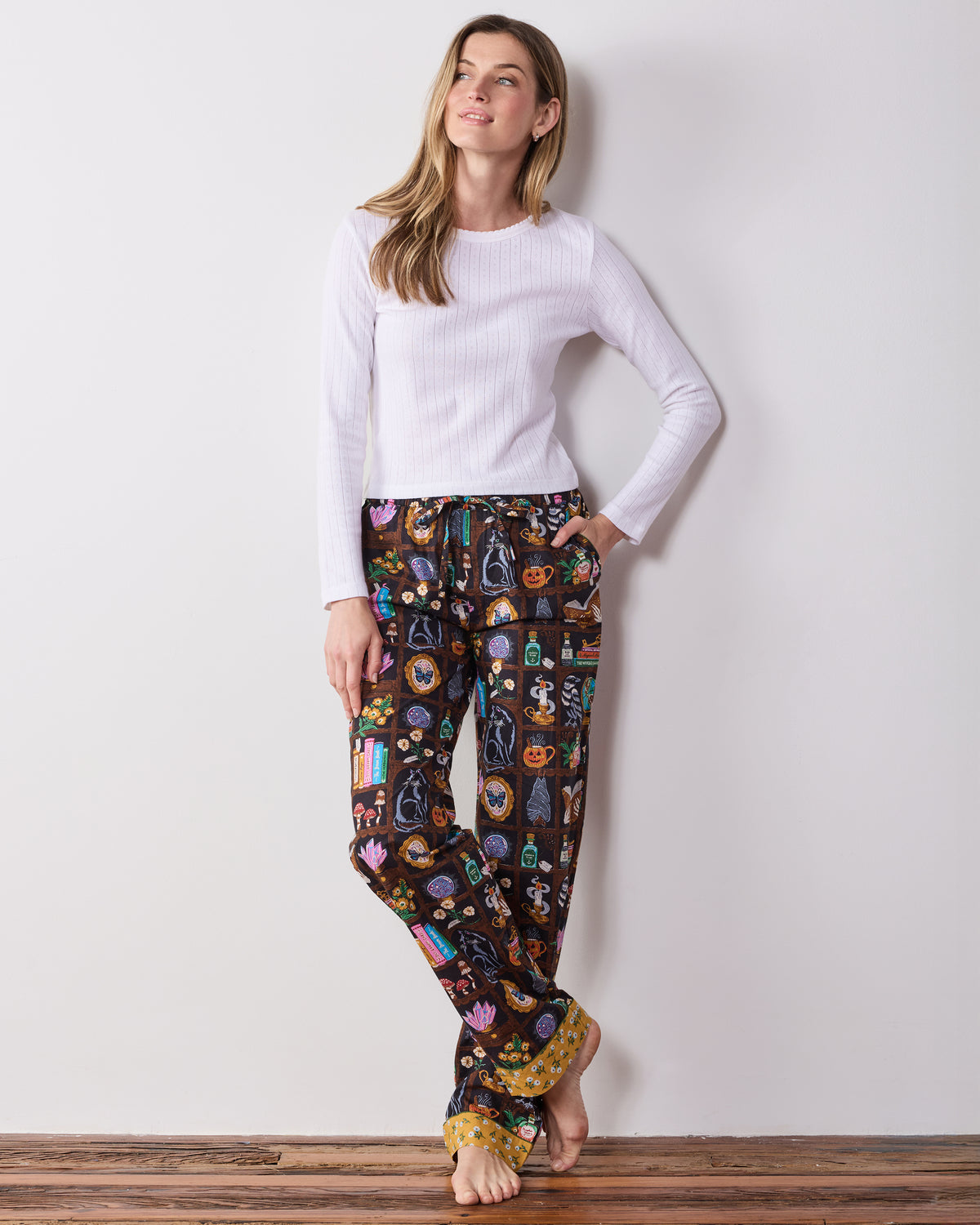 Full front view of the Enchanted Study pajama pants worn with a white long-sleeve top, showing the dark illustrated print and contrasting cuffs.