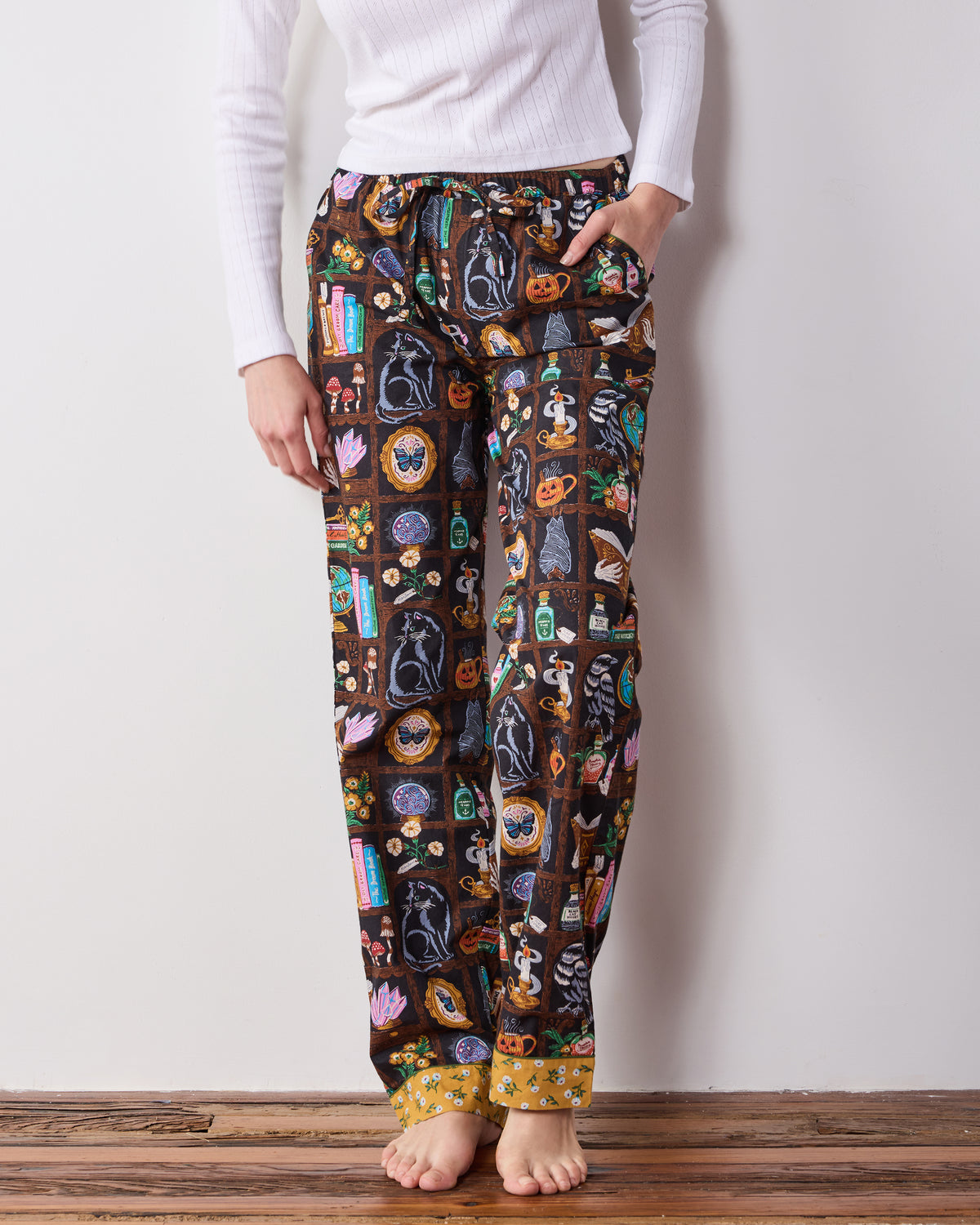 Front view of the Enchanted Study pajama pants with an elastic drawstring waist, side pockets, a cabinet-of-curiosities print, and contrasting patterned cuffs.