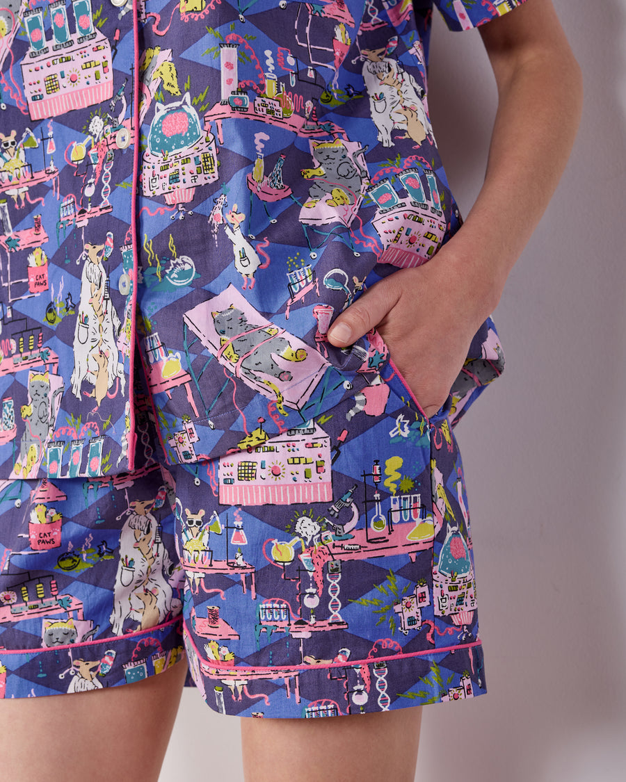 Close-up of the It's Alive pajama shorts showing a side pocket, pink piping, and colorful laboratory-themed cat-and-mouse print.