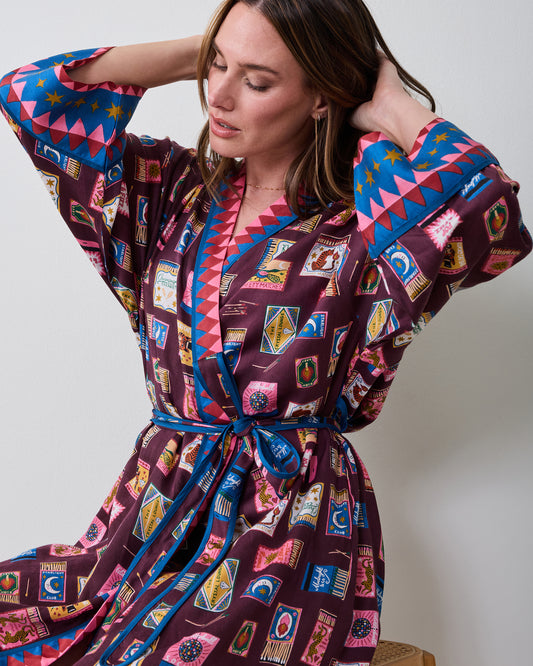 Seated front view of the Cabernet Painted Matchbook robe, showing the wrap front, tied belt, patterned fabric, and contrasting geometric trim on the collar and cuffs.