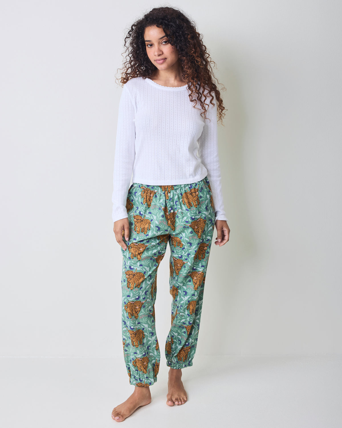 Model wearing green Highland cow-print joggers with elastic ankle cuffs, shown standing.