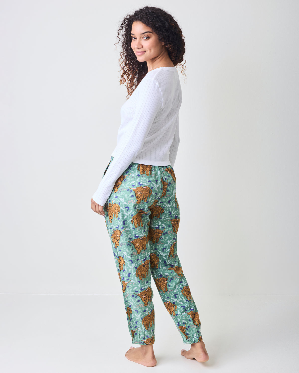 Back three-quarter view of green Highland cow-print joggers with elastic ankle cuffs