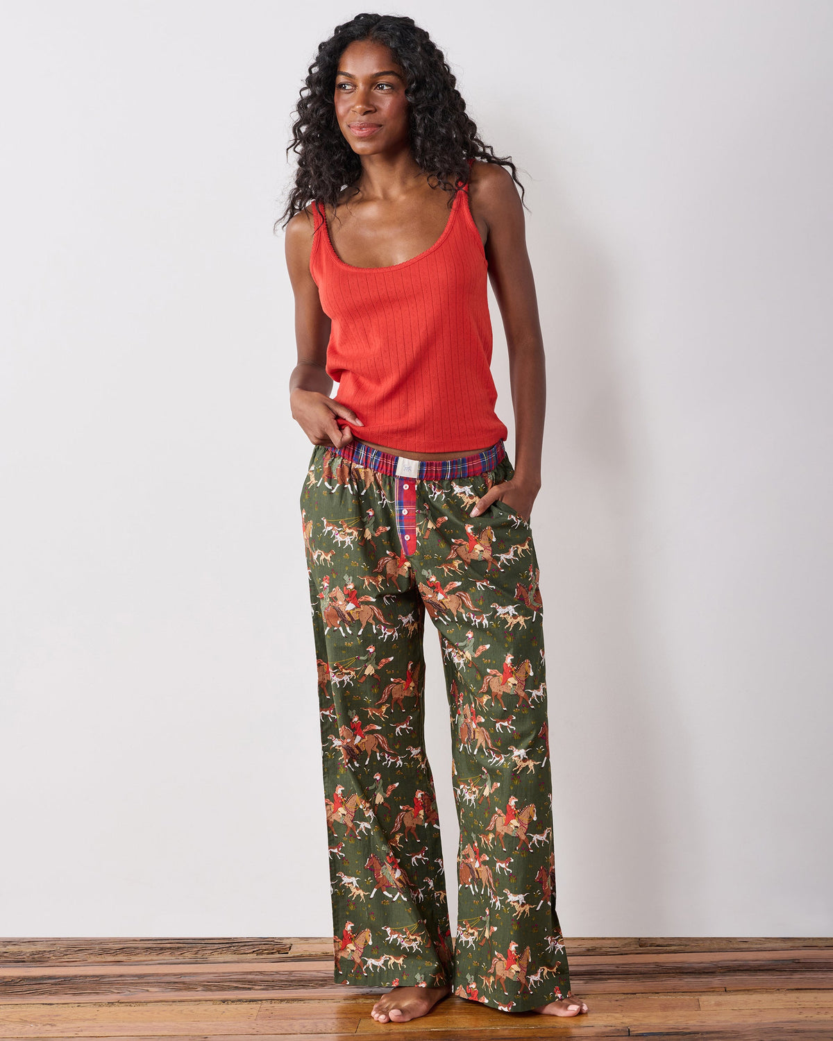 Full front view of a person wearing petite fox-and-hounds print pajama pants with a red tank top.