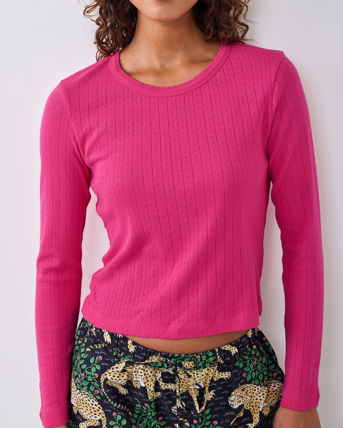 Cropped view of a bright pink long-sleeve pointelle shirt with a scalloped neckline, worn with printed pajama pants.