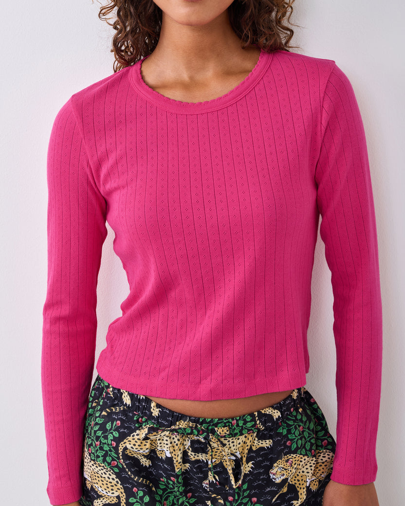 Cropped view of a bright pink long-sleeve pointelle shirt with a scalloped neckline, worn with printed pajama pants.