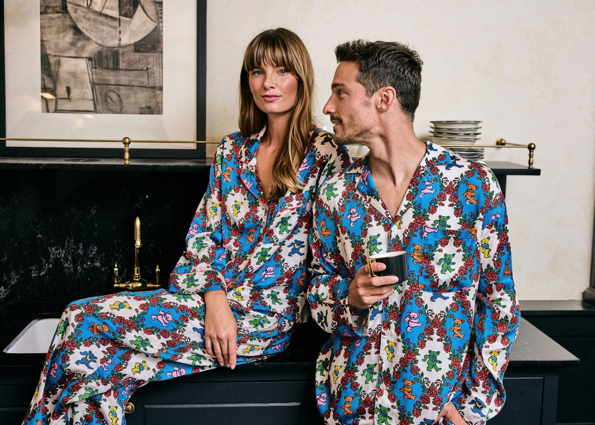 Two people wearing matching patterned clothing with colorful bear and rose motifs, seated beside a fireplace. TM & © 2026 GDP