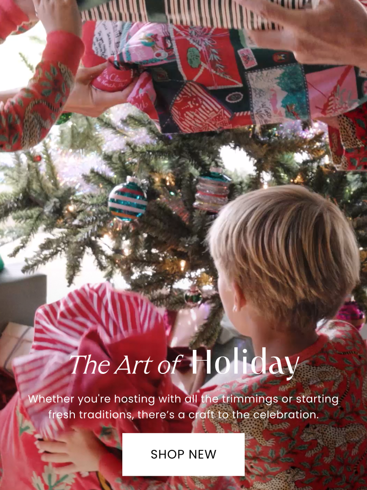 People in patterned red clothing decorate a lit Christmas tree; text reads “The Art of Holiday” and “Whether you're hosting with all the trimmings or starting fresh traditions, there's a craft to the celebration.” with a “SHOP NEW” button.