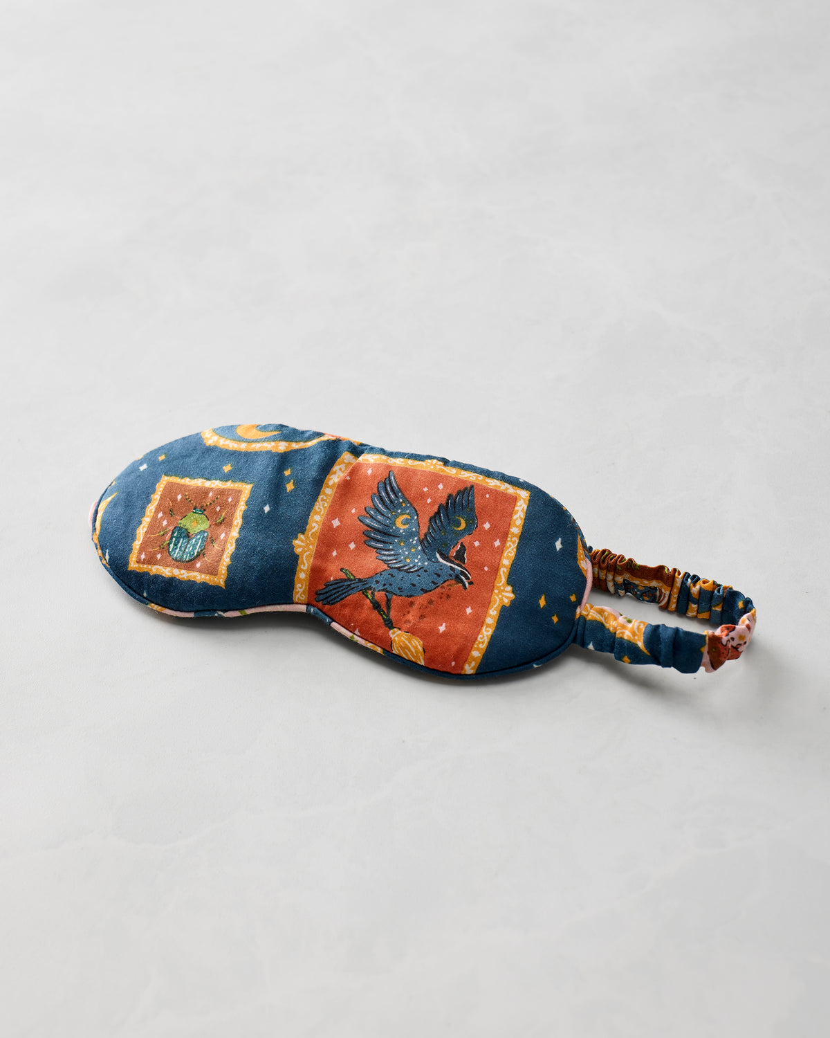 Midnight Gallery eye mask shown alone, with a dark blue framed bird print and adjustable strap.