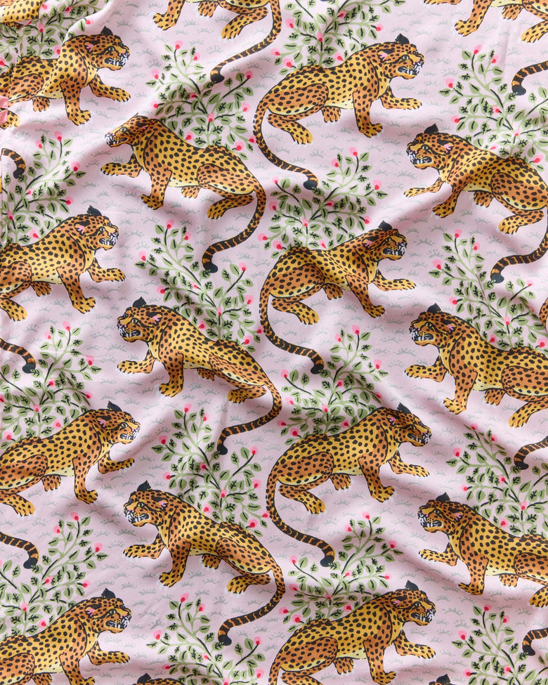 Blush fabric swatch with repeating illustrated leopards among leafy branches and pink flowers.