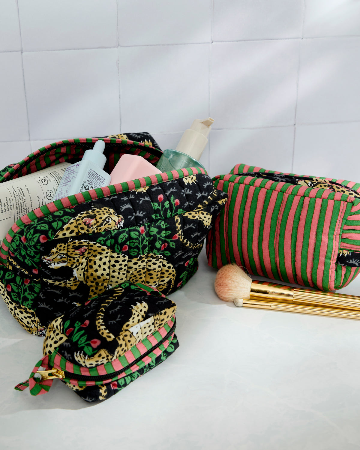 Three quilted pouches in leopard and coordinating striped prints, shown with toiletries and makeup brushes.