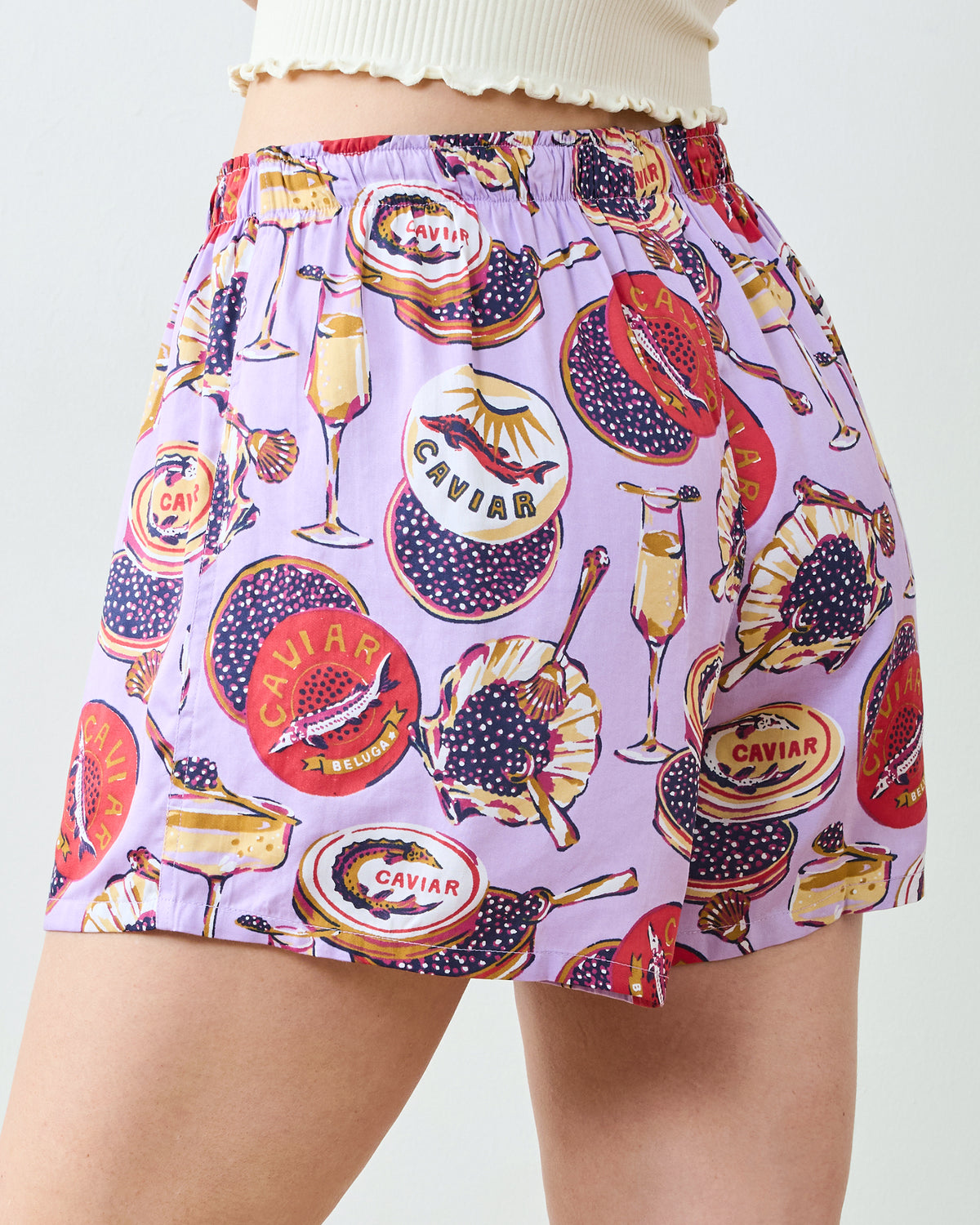 Close-up rear view of lavender boyfriend boxer shorts with champagne flute and caviar-themed print, showing the elastic waistband.